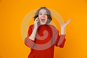 Portrait of positive woman holding and speaking on cell phone while standing isolated over yellow background