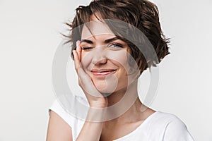 Portrait of positive woman with short brown hair in basic t-shirt smiling and touching her face with hand