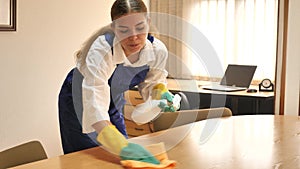 Portrait of a positive young female worker cleaning an office desk with a rag and detergent.