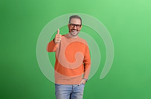 Portrait of positive young handsome entrepreneur showing thumbs up sign over green background