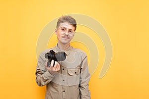 Portrait of positive young professional photographer against yellow background, standing with camera in hand and posing at camera