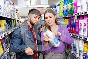 Portrait of positive young woman and man choosing liquid laundry detergents during shopping at supermarket