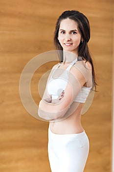 Portrait of positivity and pretty girl in white top and leggings smiling at camera and posing with crossed arms the gym. Concept o