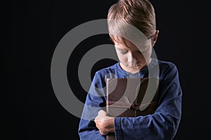Portrait of praying boy with Bible on dark background