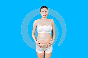 Portrait of pregnancy belt dressed on suffering pregnant woman in underwear for reducing pain in the back at blue background with