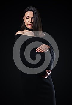 portrait of pregnant woman in black dress on black background with copy space