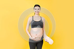 Portrait of pregnant woman putting on a bandage at yellow background with copy space. Orthopedic abdominal support belt concept
