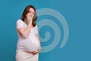 Portrait of a pregnant woman with a puzzled questioning look on a blue background