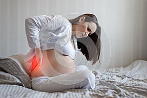 Portrait of a pregnant woman on the side of the bed holding the waist. back pain, pregnancy difficulties