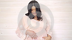 Portrait of pregnant woman stroking her belly on beige background. 4k