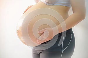 Portrait of a pregnant woman touching her belly with hands.