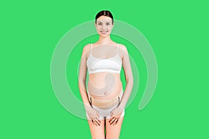 Portrait of pregnant woman in underwear wearing elastic maternity band at green background with copy space. Orthopedic abdominal