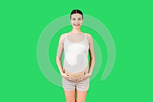 Portrait of pregnant woman using pregnancy belt at green background with copy space. Orthopedic abdominal support belt concept