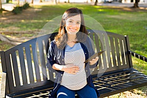 Portrait of a pregnant woman using a tablet in the park