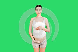 Portrait of pregnant woman wearing pregnancy corset against backpain at green background with copy space. Orthopedic abdominal