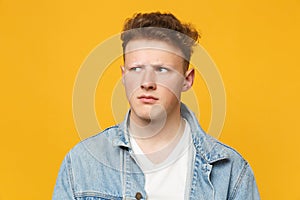 Portrait of preoccupied pensive young man wearing denim casual clothes looking aside isolated on yellow orange wall