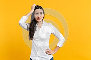 Portrait of preoccupied pensive young woman in white shirt looking aside, putting hand on head isolated on bright yellow