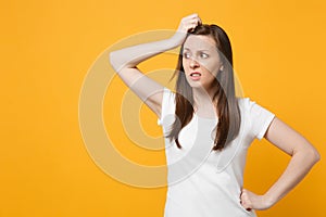 Portrait of preoccupied young woman in white casual clothes looking aside putting hand on head isolated on bright yellow