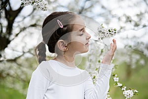 Portrait of preschool girl against white blloming tree in spring