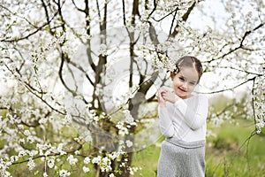 Portrait of preschool girl against white blloming tree in spring