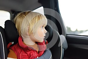 Portrait of a preschooler boy sitting in a car seat and wearing a belt. Ð¡hild is looking out the window of a car during a family