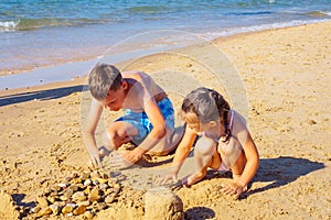 Portrait of preteen boy brother, little girl family sitting on beach seashore, playing with sand, building castles.