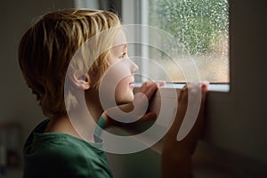 Portrait of preteen boy standing at the window. Child watching the rain outside