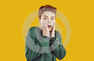 Portrait of preteen boy who is funny scared and grabs his face on orange background.