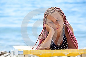 Portrait of preteen girl with pink dreadlocks hairstyle tanning on beach on seacoast