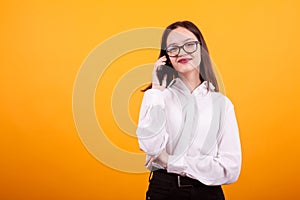 Portrait of prett young girl taking on the phone and looking at the camera over yellow background