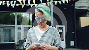 Portrait of pretty Asian punk girl using smartphone touching screen outdoors