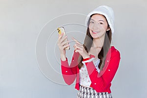 Portrait of a pretty Asian teen girl wearing a red dress and white hat happily smile using a smartphone on a white background