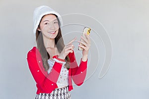 Portrait of a pretty Asian teen girl wearing a red dress and white hat happily smile using a smartphone on a white background