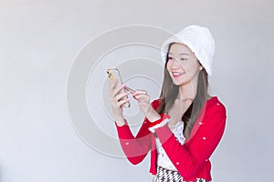 Portrait of a pretty Asian teen girl wearing a red dress and white hat happily using a smartphone on a white background