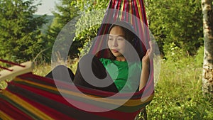 Portrait of pretty asian woman hiker in headphones enjoying music and relaxing in hammock outdoors.