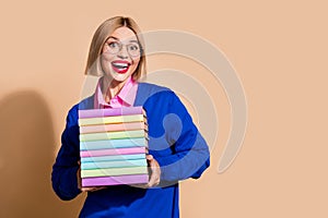 Portrait of pretty astonished girl toothy smile hands hold pile stack book empty space ad isolated on beige color