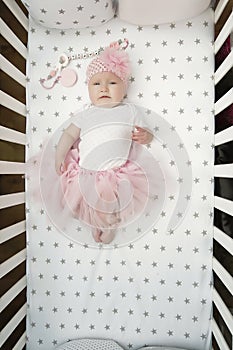 Portrait of pretty baby girl with fluffy pink skirt and a flower on her head. smart kid