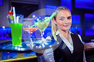 Portrait of pretty bartender holding serving tray with cocktails