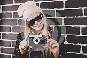 Portrait of pretty blond hair smileing young teenage hipster woman model with retro photo camera wearing a pink hat