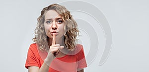 Portrait of pretty blonde girl holding index finger on lips. Silence and secret concept. Copy space