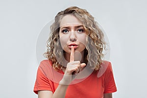 Portrait of pretty blonde girl holding index finger on lips. Silence and secret concept. Studio shot, white background
