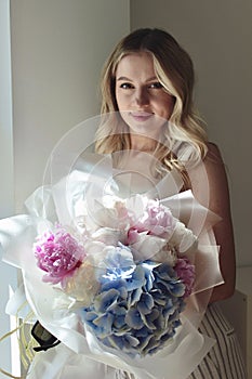 Portrait of a pretty blonde with long hair and a delicate bouquet of peonies