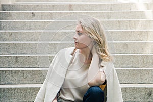 Portrait of a pretty blue eyed blonde girl sitting on the steps with her hand holding her neck