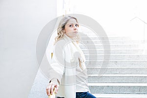 Portrait of a pretty blue eyed blonde girl in a white jacket with a serious face looks at the camera