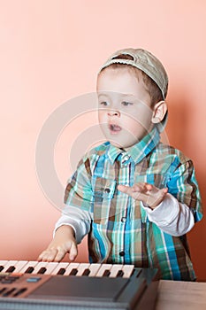 Cute boy wearing baseball cap backwards playing the digital piano