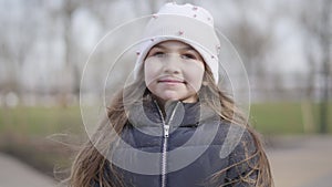 Portrait of pretty brunette Caucasian girl laughing and talking outdoors. Close-up face of cheerful cute kid enjoying