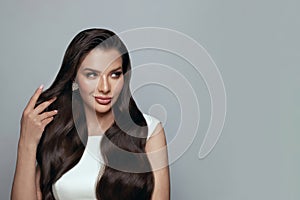 Portrait of pretty brunette woman with long wavy hairstyle smiling and touÑhing her hair on white background.