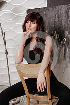 Portrait of a pretty brunette woman sits on a chair on a gray background