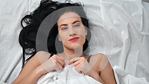 Portrait of pretty brunette young smiling woman lying on bed. Medium close up shot on pillow RED camera