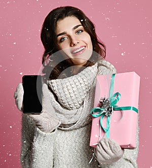 Portrait of a pretty casual girl holding gift box and showing blank screen mobile phone